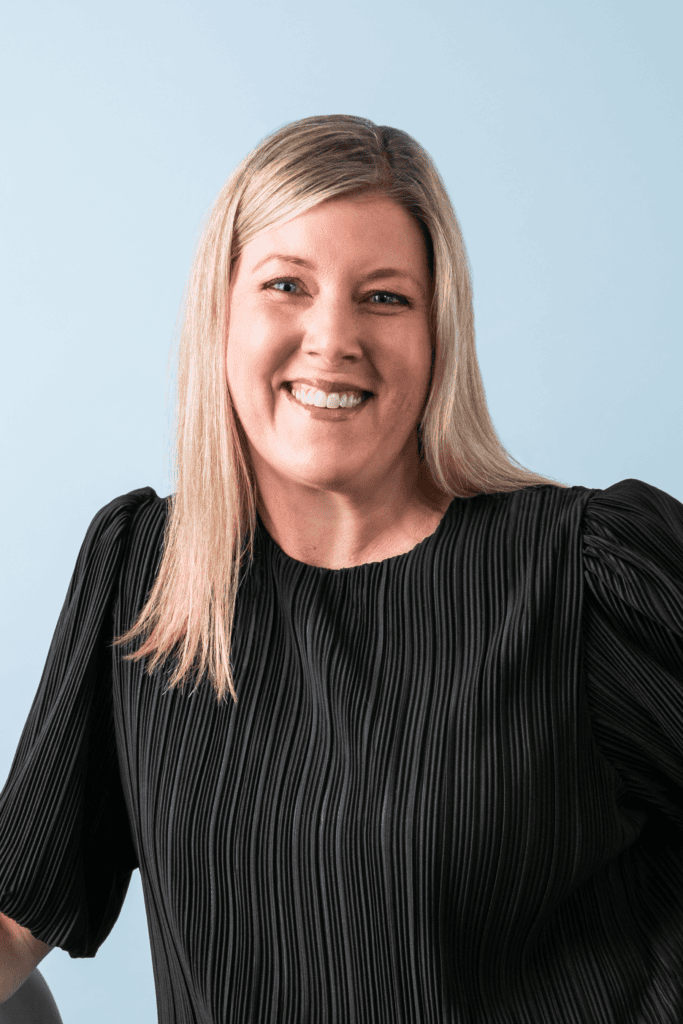 Business headshot of Heather Deschenes, Vice President of North America Marketing, Vistaprint. Caucasian female with blonde hair wearing black blouse and smiling