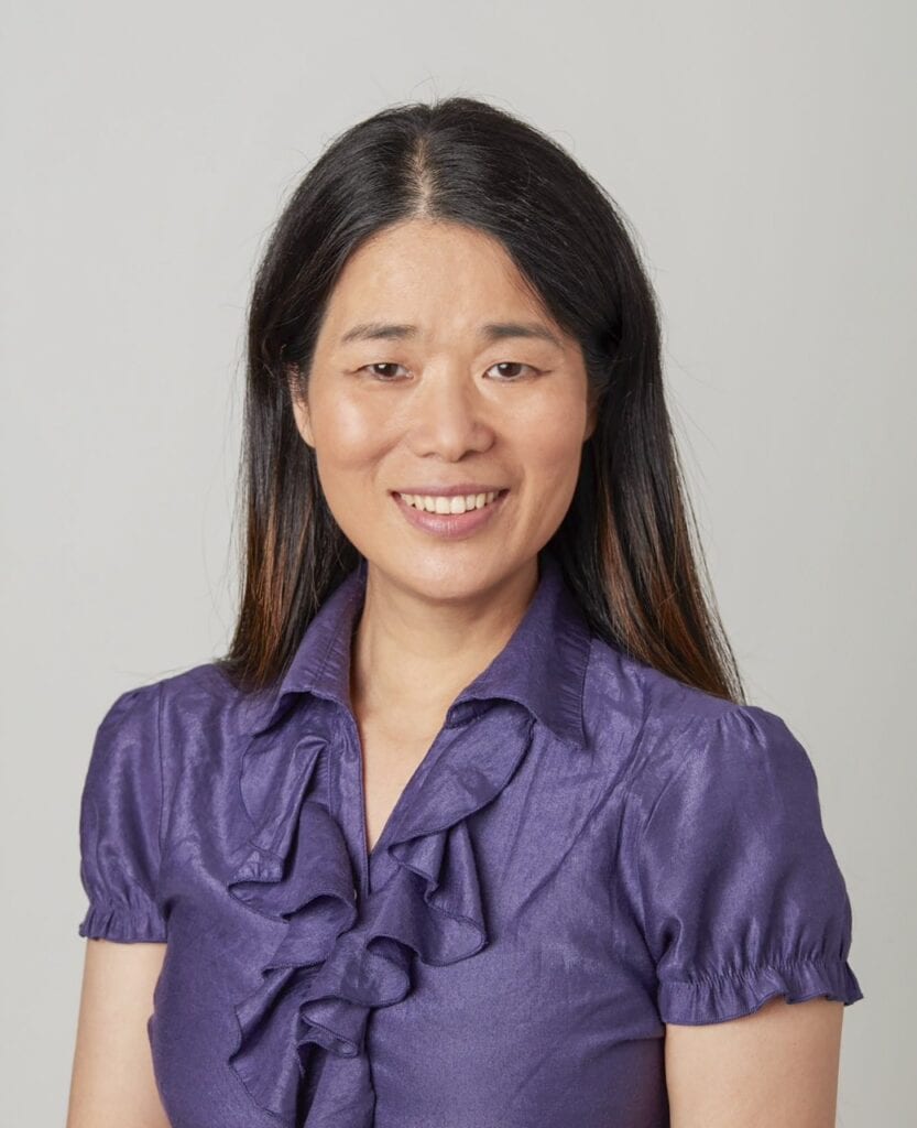 Business headshot of Asian woman, Yushuang Zhou, wearing purple blouse. She has brown eyes and brown hair parted down the middle and is smiling.